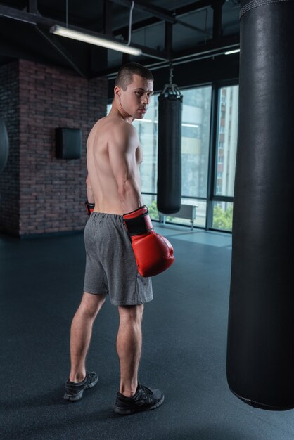 Big window. Professional famous boxer with nice athletic body standing near big window with city view