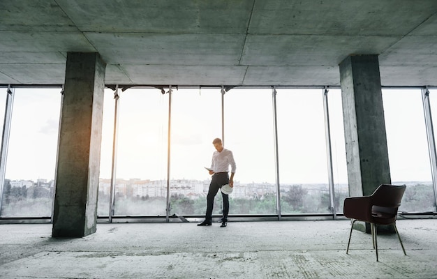 Big window Young man in formal wear is working indoors on the construction