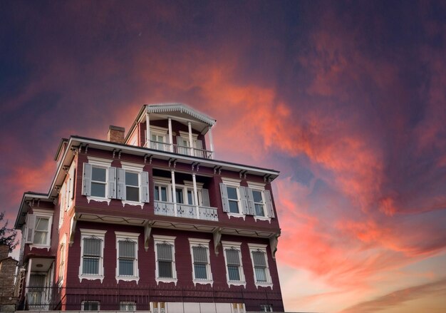 Big wooden house on the background of the red sky at sunset.  Big wooden mansion and red cloudy sky,