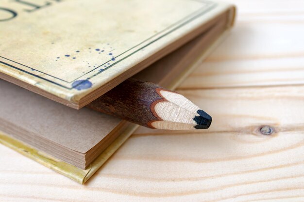 A big wooden pencil sticking out of a notepad with craft paper sheets lying on a wooden background