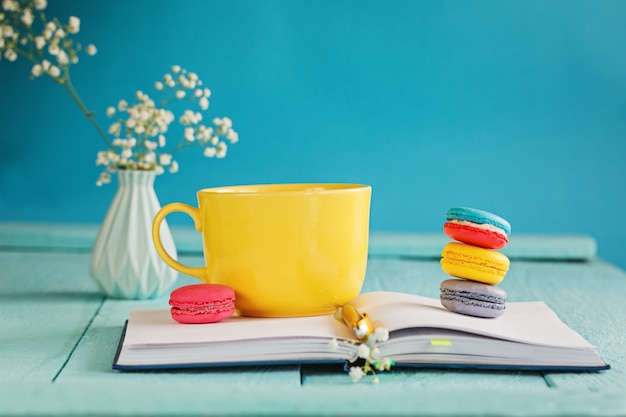 Big yellow cup of tea with flower and macaroons and notebook on blue