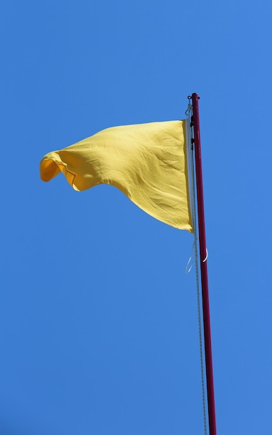 Photo big yellow flag symbol of danger of warning and the blue sky on background