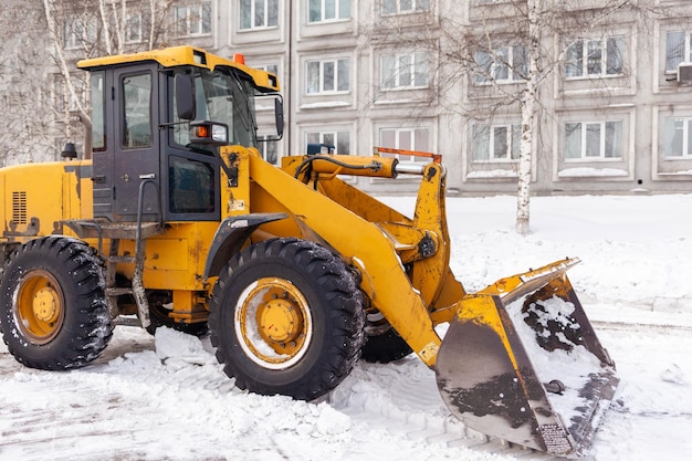 A big yellow tractor removes snow from the roadCleaning of roads in the city from snow in winter