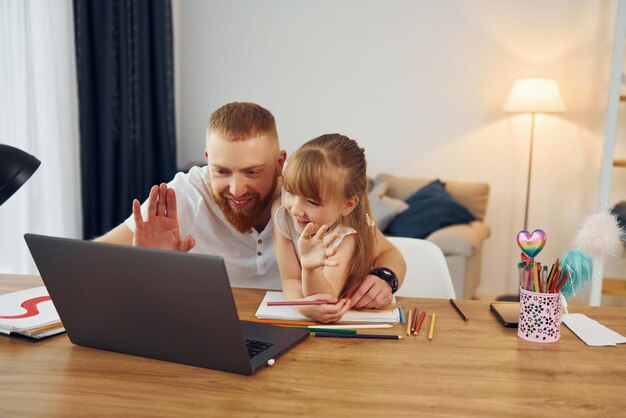 Bij de tafel met laptop erop Vader met zijn dochtertje is samen thuis