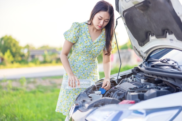 Bij het repareren van haar kapotte auto giet een jonge vrouw water voor het wassen van glazen in haar auto.