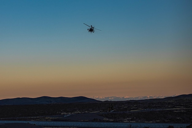 Bij zonsondergang vliegt een helikopter over de bergen.