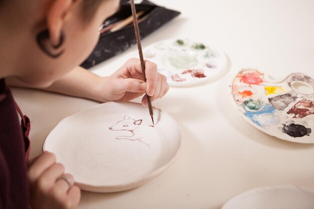 Bijgesneden achteraanzicht close-up van een vrouwelijke kunstenaar die op een keramische plaat schildert