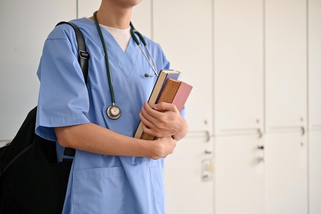 Bijgesneden afbeelding een aziatische mannelijke geneeskundestudent in een uniform met zijn medische boeken en rugzak