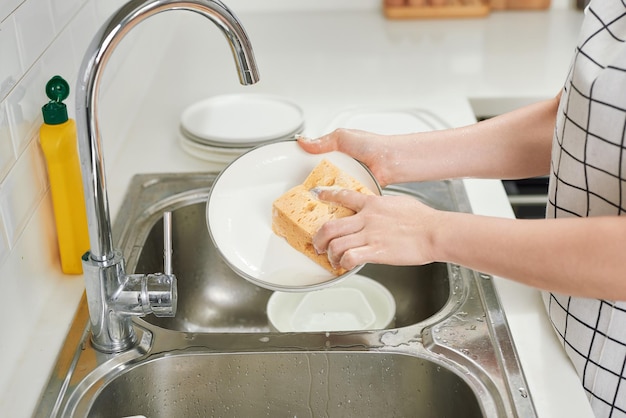 Bijgesneden afbeelding van aantrekkelijke jonge vrouw is afwassen terwijl ze thuis schoonmaakt