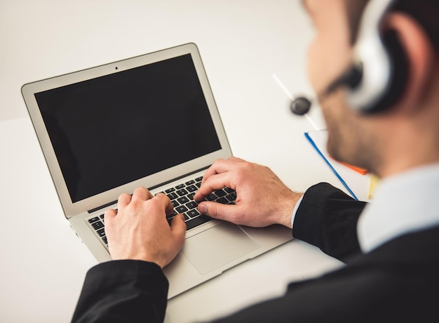 Bijgesneden afbeelding van aantrekkelijke zakenman in pak en headset werken met laptop op kantoor