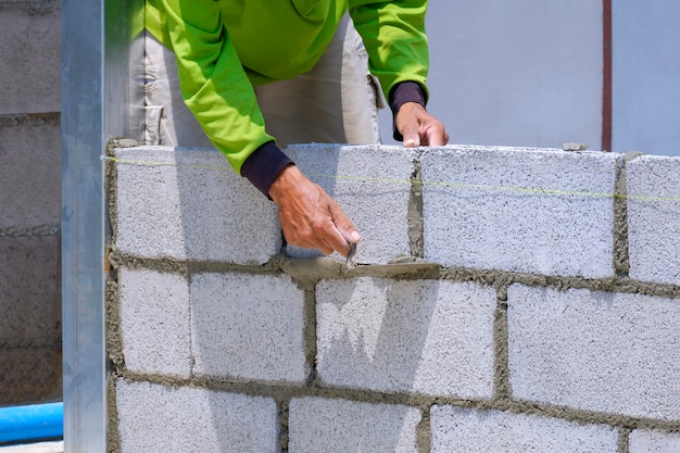 Bijgesneden afbeelding van Aziatische bouwvakker die betonnen blokmuur bouwt op de bouwplaats van het huis