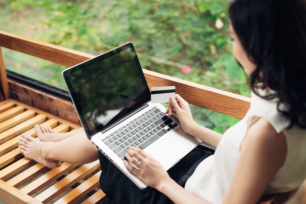 Bijgesneden afbeelding van Aziatische vrouw die online winkelt terwijl ze bij het raam zit in een creatief kantoor of café