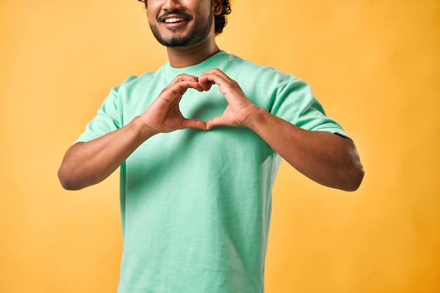 Bijgesneden afbeelding van een Indiase man in een turquoise T-shirt met een gebaar van liefde, genegenheid en zorg met zijn vingers