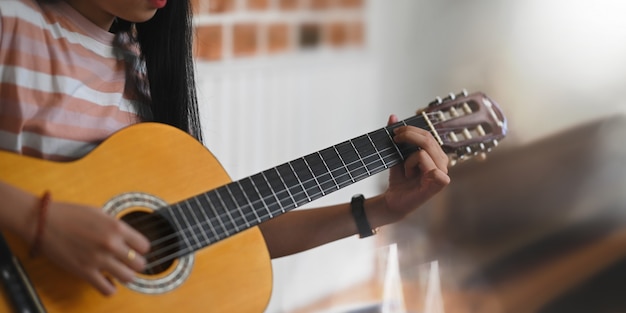 Bijgesneden afbeelding van een jonge aziatische vrouw oefent haar vaardigheid op akoestische gitaar