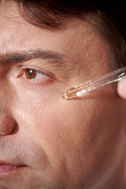 Bijgesneden afbeelding van een man van middelbare leeftijd die serum op zijn gezicht aanbrengt