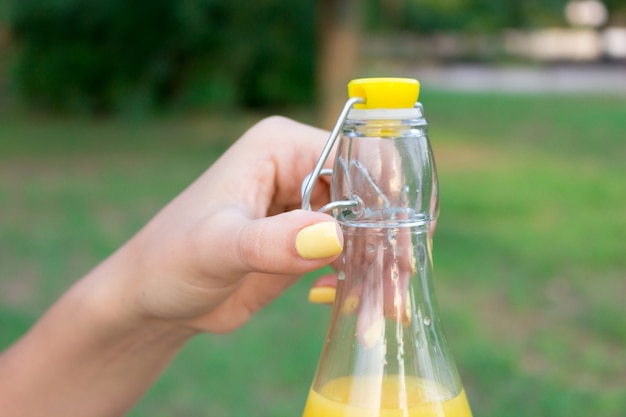 Bijgesneden afbeelding van een meisje dat buiten een fles vers sap vasthoudt en opent.