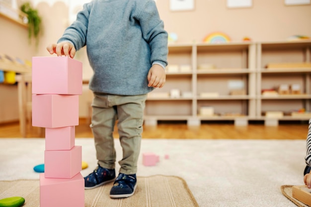 Bijgesneden afbeelding van een peuter die staat en een toren maakt van houten blokken op de Montessori-kleuterschool