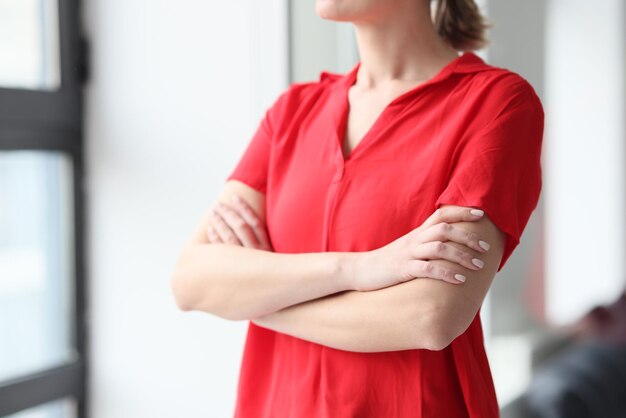 Bijgesneden afbeelding van een vrouw in een rood shirt die bij het raam staat. Vrouwelijke manager kijkt niet op kantoor