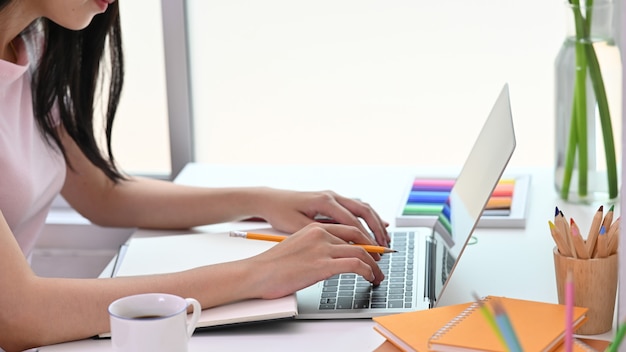 Bijgesneden afbeelding van een vrouw werkt met een computer laptop aan het witte bureau.