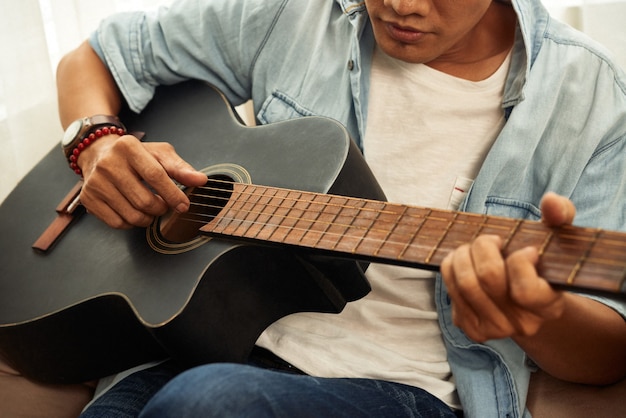 Bijgesneden afbeelding van getalenteerde creatieve jongeman die thuis gitaar speelt