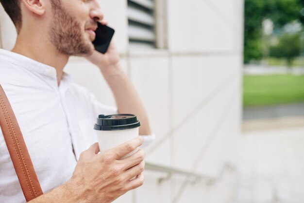Bijgesneden afbeelding van jonge bebaarde man kopje koffie drinken en praten over de telefoon