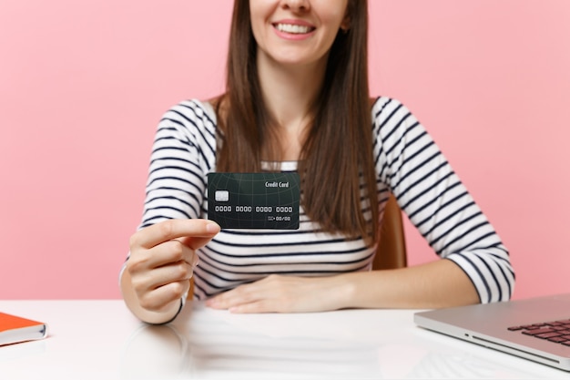 Bijgesneden afbeelding van jonge lachende vrouw in vrijetijdskleding met creditcardwerk zit aan een wit bureau