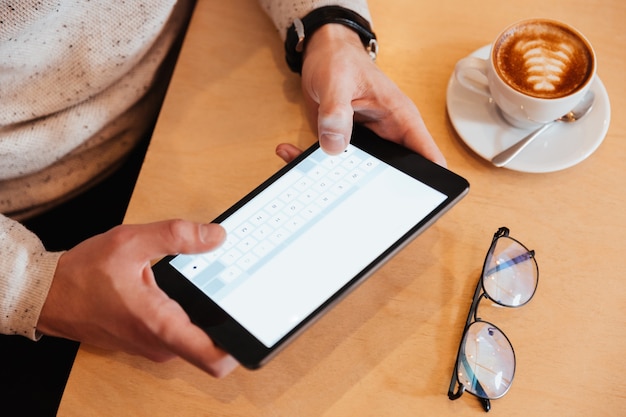 Bijgesneden afbeelding van jonge man zit in café tijdens het gebruik van tablet pc.