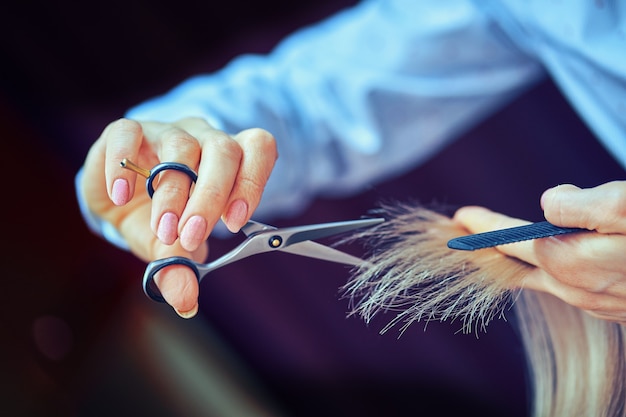 Bijgesneden afbeelding van kapper die uiteinden van blond haar trimt