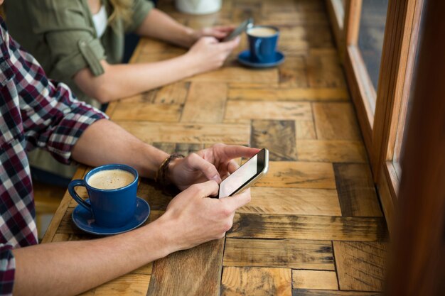 Bijgesneden afbeelding van man en vrouw met behulp van mobiele telefoons in coffeeshop