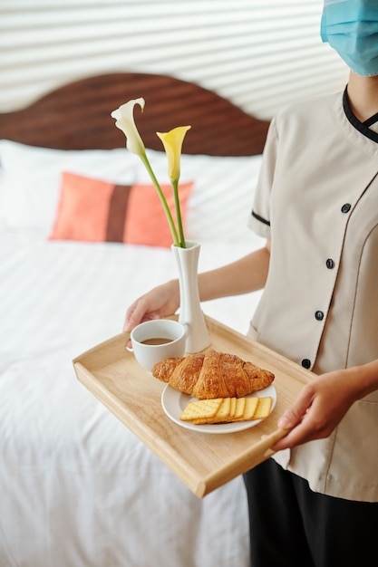 Bijgesneden afbeelding van meid die verse koffie, croissants en koekjes in de hotelkamer van de gast brengt