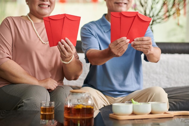 Bijgesneden afbeelding van senior man en vrouw met rode enveloppen met geluksgeld