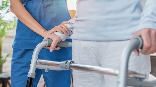 Bijgesneden afbeelding van verpleegster die oudere vrouw helpt thuis met rollator te lopen