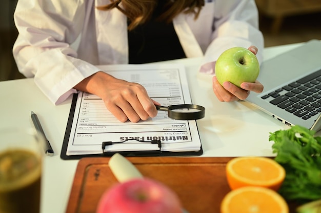 Bijgesneden afbeelding van voedingsdeskundige die een appel vasthoudt en recept voorschrijft aan een bureau met vers fruit Gezondheidszorg en dieetconcept