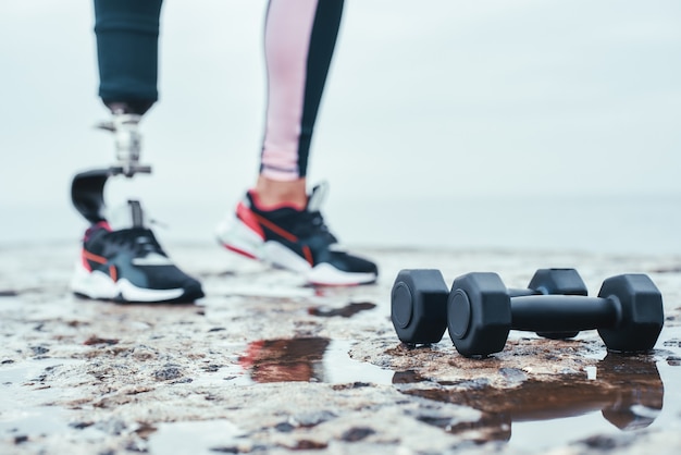 Foto bijgesneden afbeelding van vrouw met beenprothese en halters liggend voor de zee