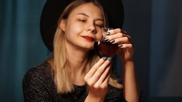 Bijgesneden afbeelding van vrouw met hartvormige glazen pot liefdesdrankje. mooie jonge vrouw in een heksenhoed. focus op potion of poison vial