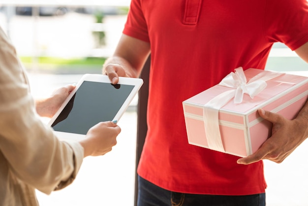 Bijgesneden beeld van bezorger die roze cadeau houdt en digitale tablet aan vrouw geeft