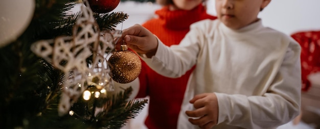 Bijgesneden beeld van gelukkige jongen die kerstboom versiert met zijn moeder tijdens gezellige huisavond