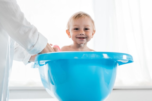 Bijgesneden beeld van moeder die een gelukkig peuterkind wast in een blauw babybadje