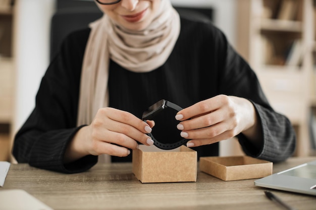 Bijgesneden beeld van moslimvrouw die livestream doet terwijl ze de doos uitpakt met een nieuw smartwatch