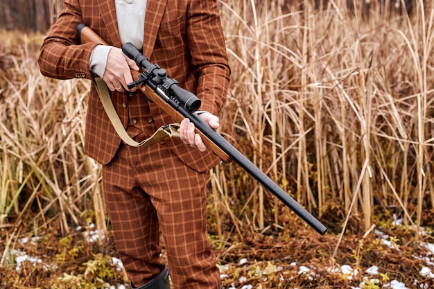 Bijgesneden blanke jager man met pistool en wandelen in het bos. Rifle Hunter In landelijk gebied. Herfst jacht. Jagen in de bergen. Een jager met jachtgeweer, klaar om te schieten, in bruin stijlvol pak