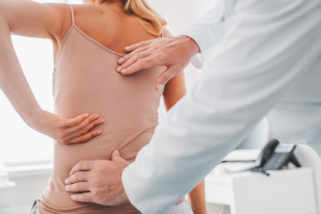 Bijgesneden close-up van mannelijke orthopedist die de rug van de patiënt in de kliniek onderzoekt