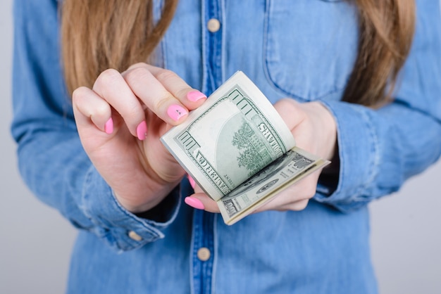 Bijgesneden close-up van meisjesachtig mooie handen met lange nagels roze heldere manicure op vingers houden berekenen oud geld dragen denim kleding geïsoleerde grijze muur