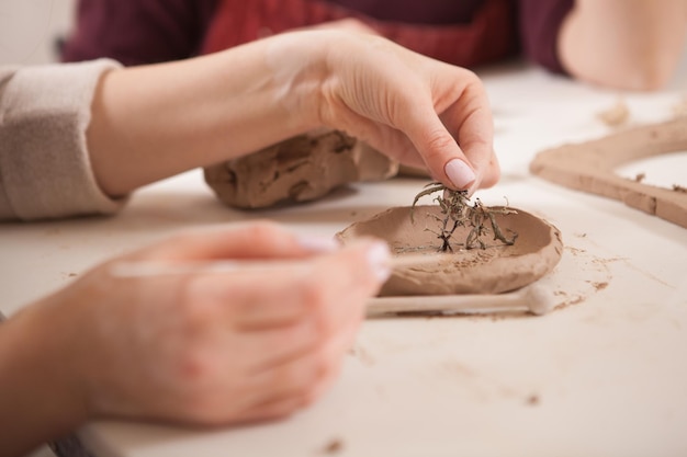 Bijgesneden close-up van onherkenbare vrouw die kleine kleiplaat decoreert in de keramiekworkshop