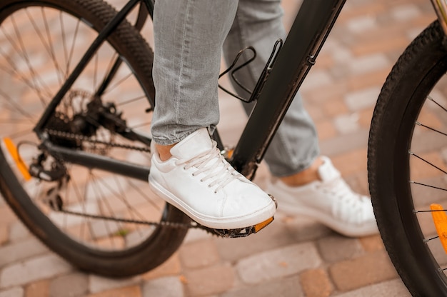 Bijgesneden foto van een blanke fietser in de sportschoenen die langs een betegeld fietspad trapt