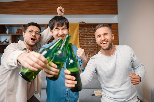 Bijgesneden foto van een flesje bier in mannenhanden die naar een voetbalwedstrijd kijken