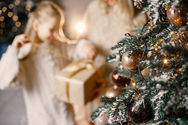 Bijgesneden foto van een klein meisje dat thuis bij de kerstboom staat met haar moeder