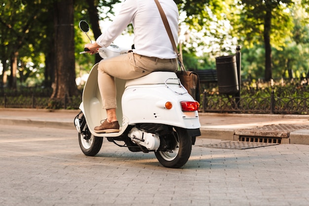 Bijgesneden foto van een knappe jonge zakenman die buiten op de scooter loopt.