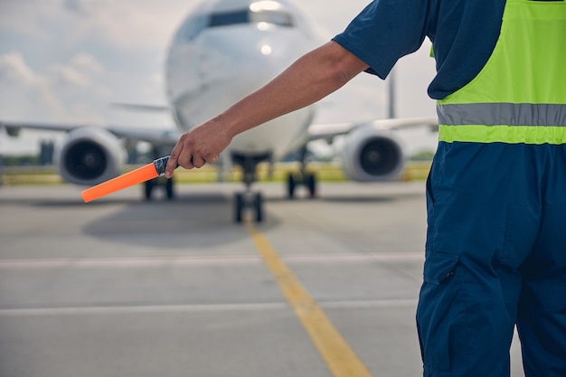 Bijgesneden foto van een luchthavenmedewerker in uniform met een rangeerstaf in één hand