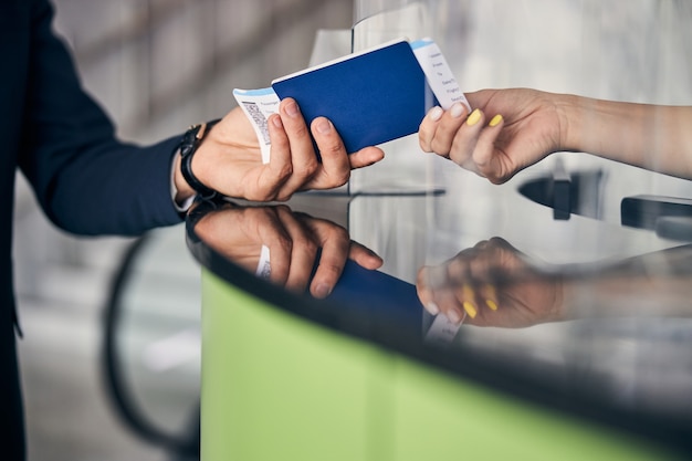 Bijgesneden foto van een paspoort en vliegtickets die door de passagiers worden doorgegeven aan een lid van het luchthavenpersoneel