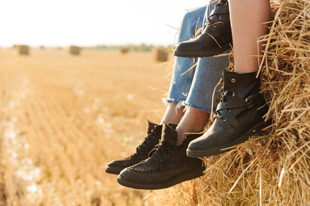 Bijgesneden foto van jonge man en vrouw zittend op grote hooiberg in gouden veld, tijdens zonnige dag